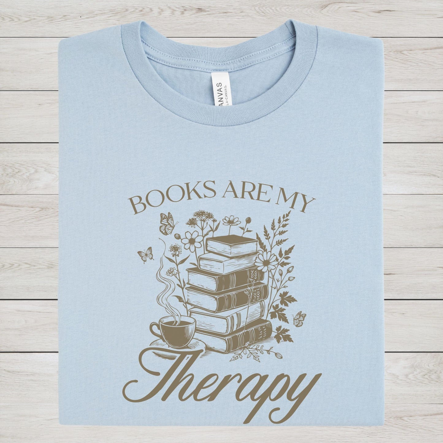 Light blue t-shirt with 'Books are my Therapy' design on a wooden surface