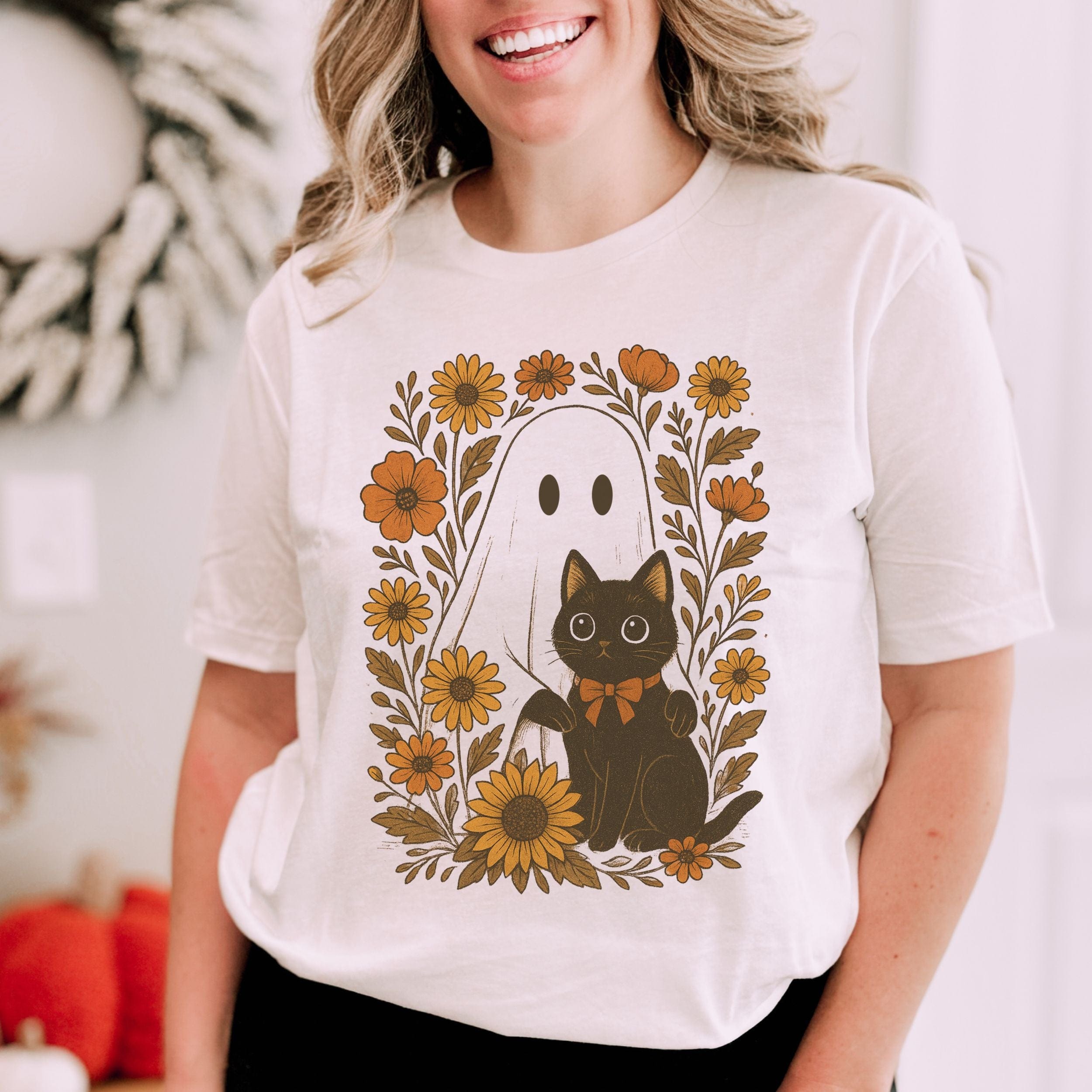 Person wearing a white t-shirt with a black cat and ghost design surrounded by flowers.