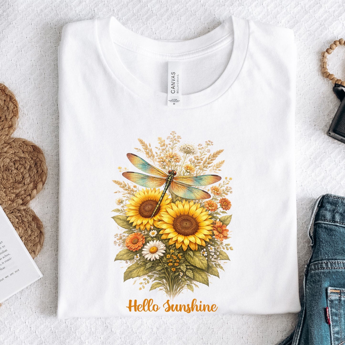 White t-shirt with a floral design featuring sunflowers and a dragonfly on a textured surface.