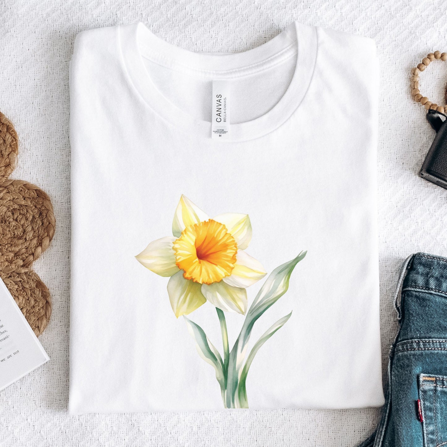 White t-shirt with a yellow flower design on a light gray surface.