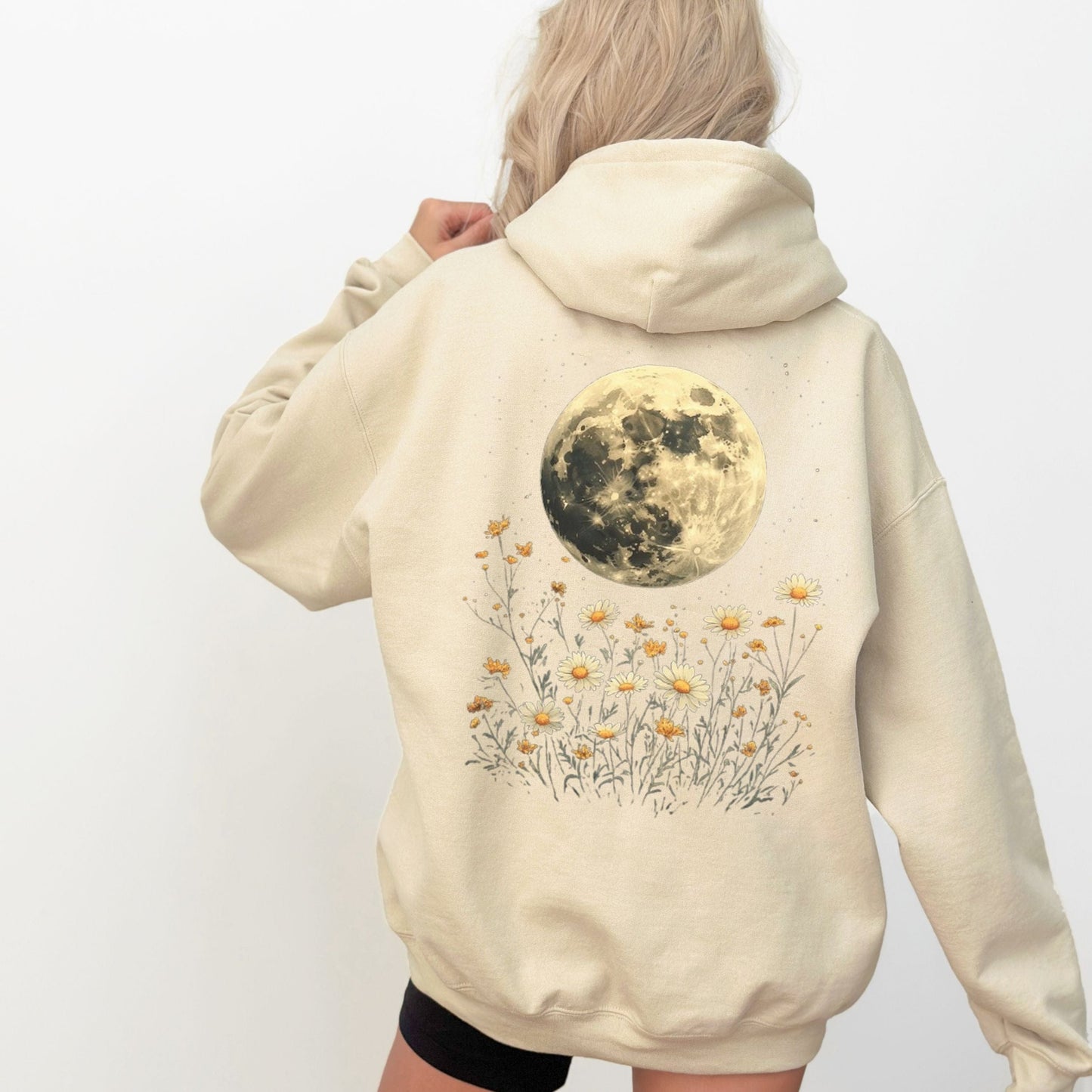 Beige hoodie with a moon and floral design on the back, worn by a person.