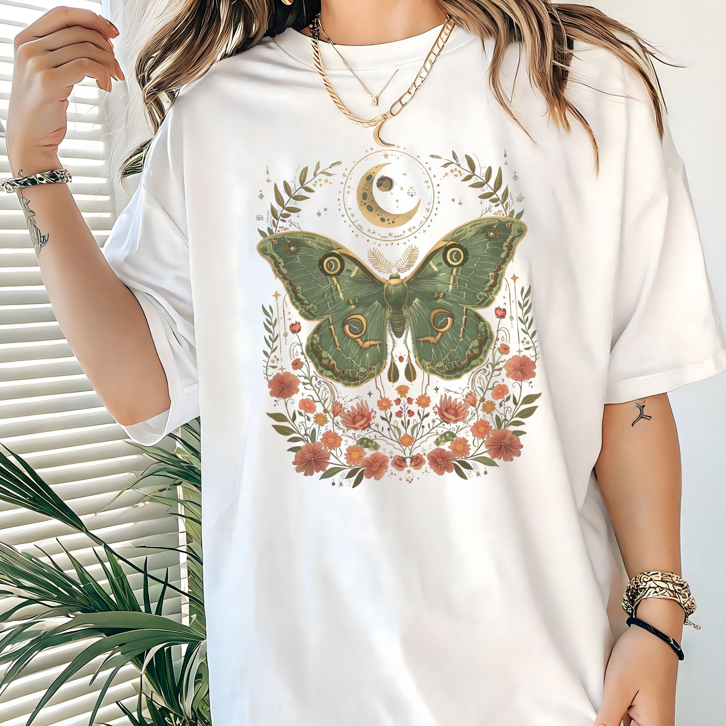 White t-shirt with a green moth and floral design worn by a person.