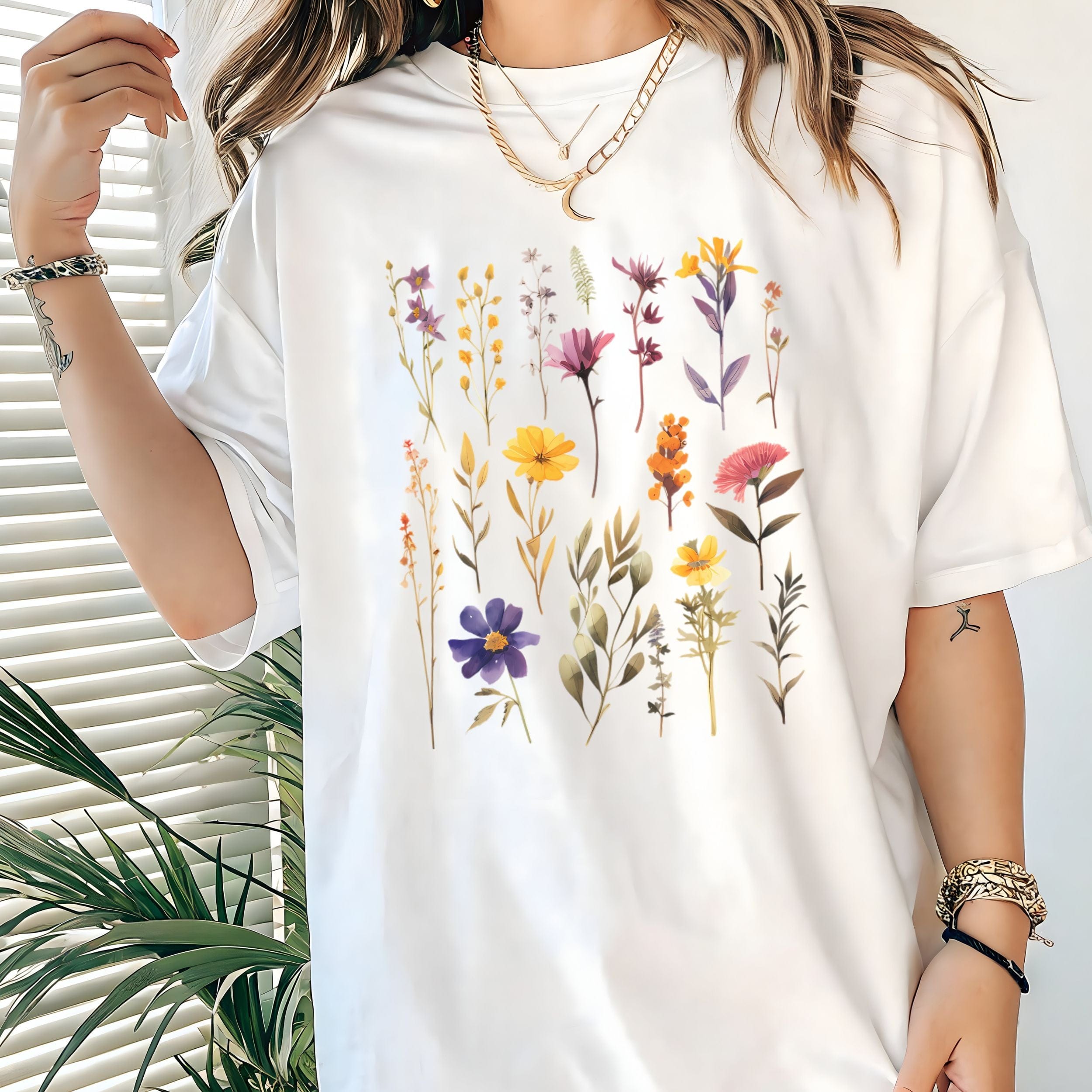 White t-shirt with floral design worn by a person, with a plant in the background.