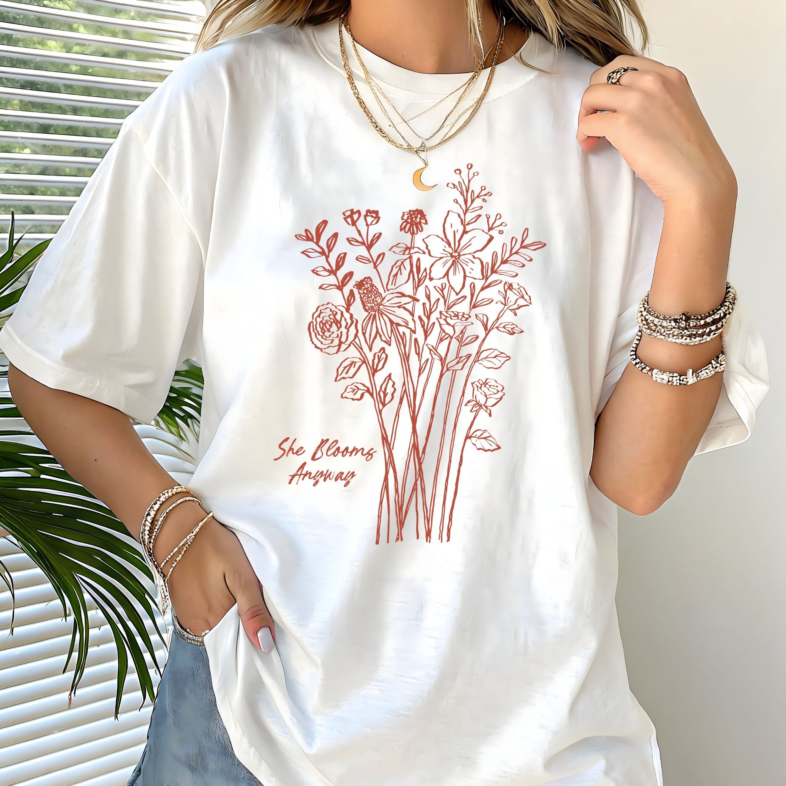 White t-shirt with floral design and text worn by a person, with a plant in the background.