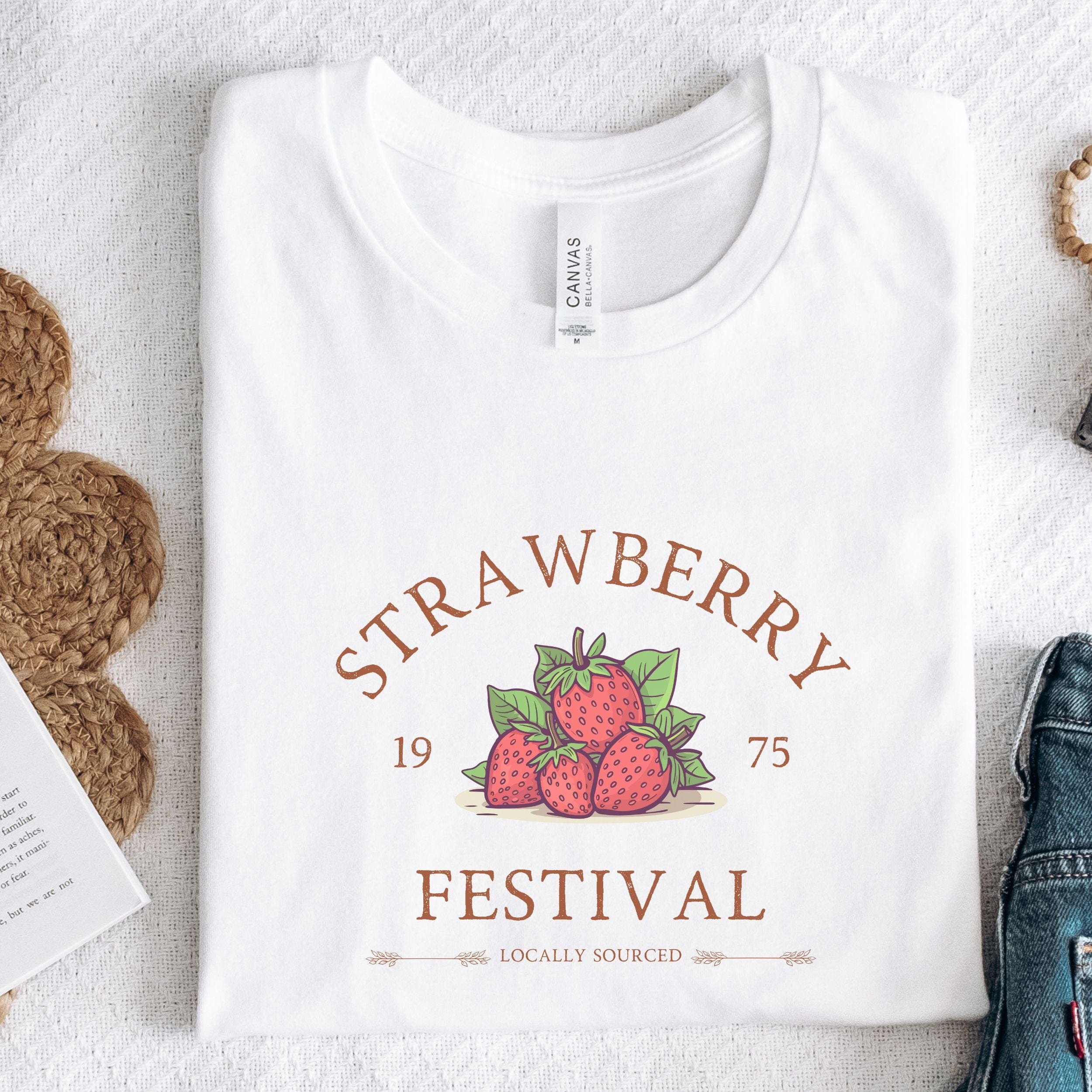 White t-shirt with 'Strawberry Festival' design on a textured surface.