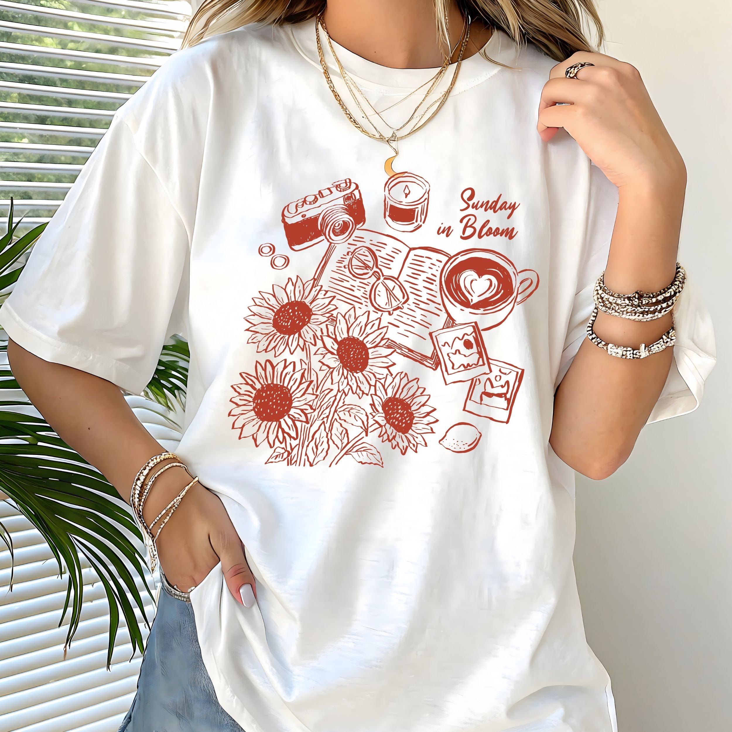 White t-shirt with red graphic design featuring sunflowers, a camera, and text, worn by a person.