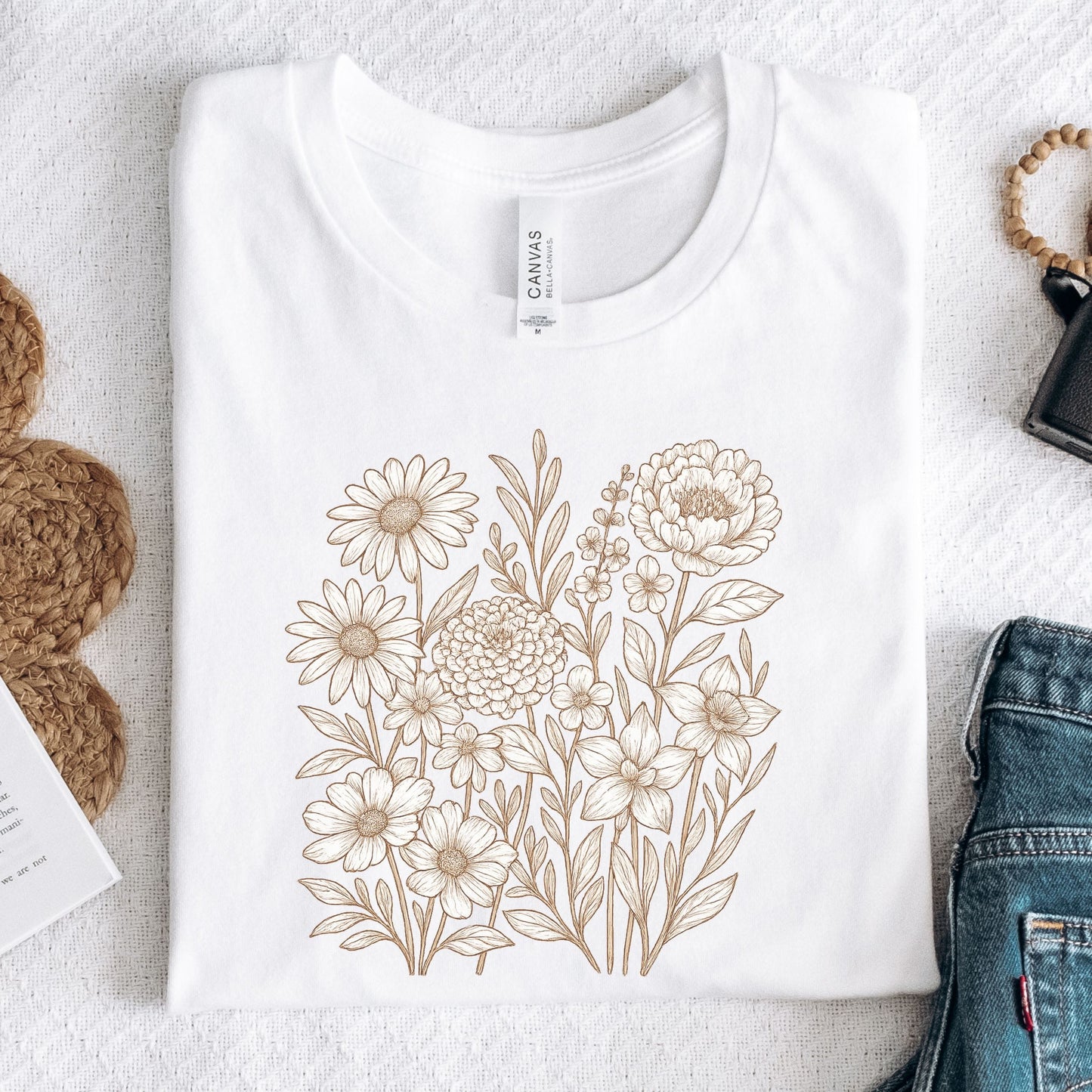 White t-shirt with floral design on a textured surface with accessories.