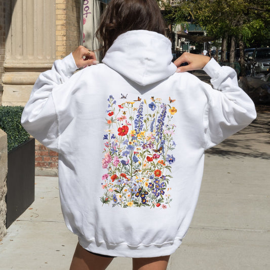 Person wearing a white hoodie with floral designs on the back, standing outdoors.
