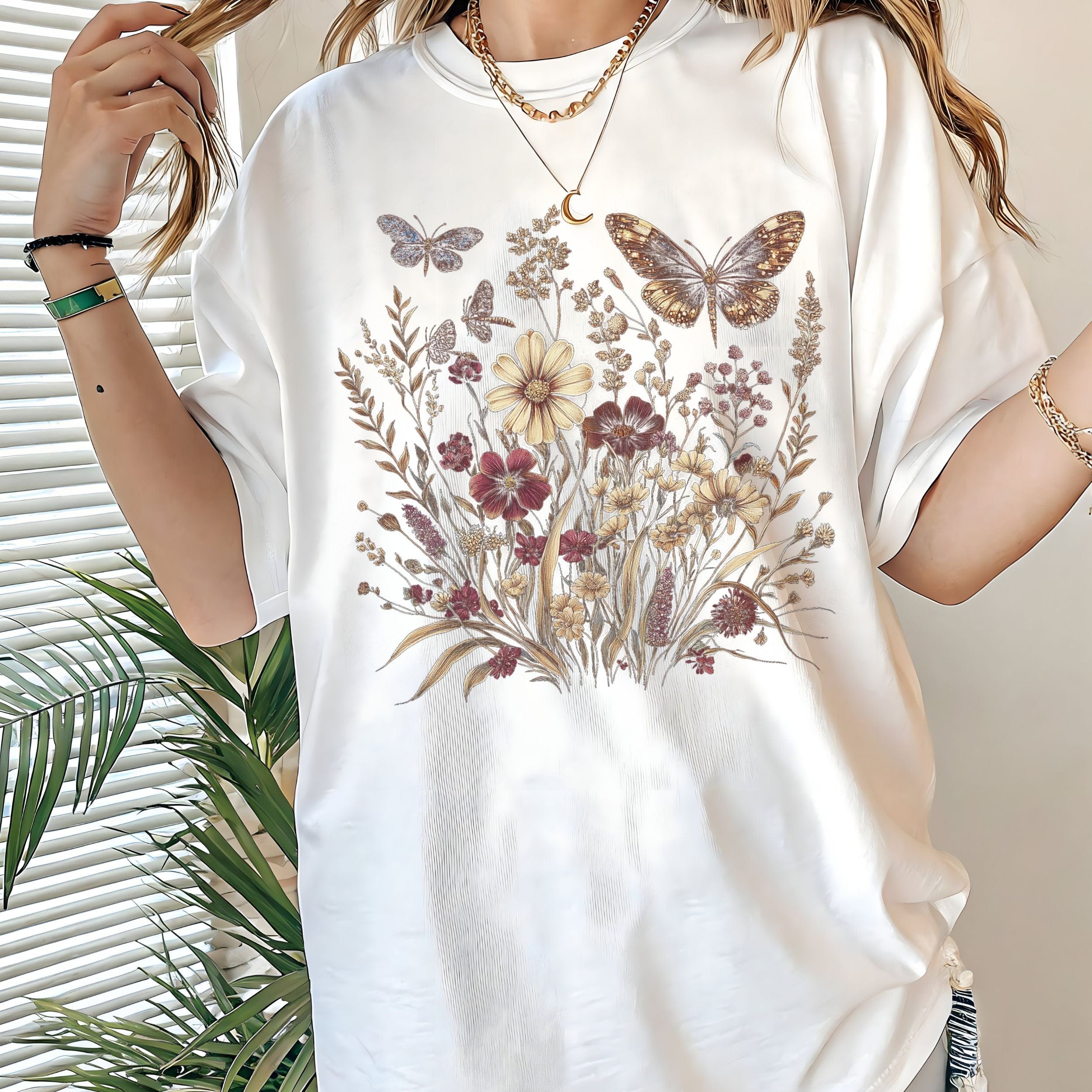 White t-shirt with floral and butterfly design worn by a person, with a plant in the background.