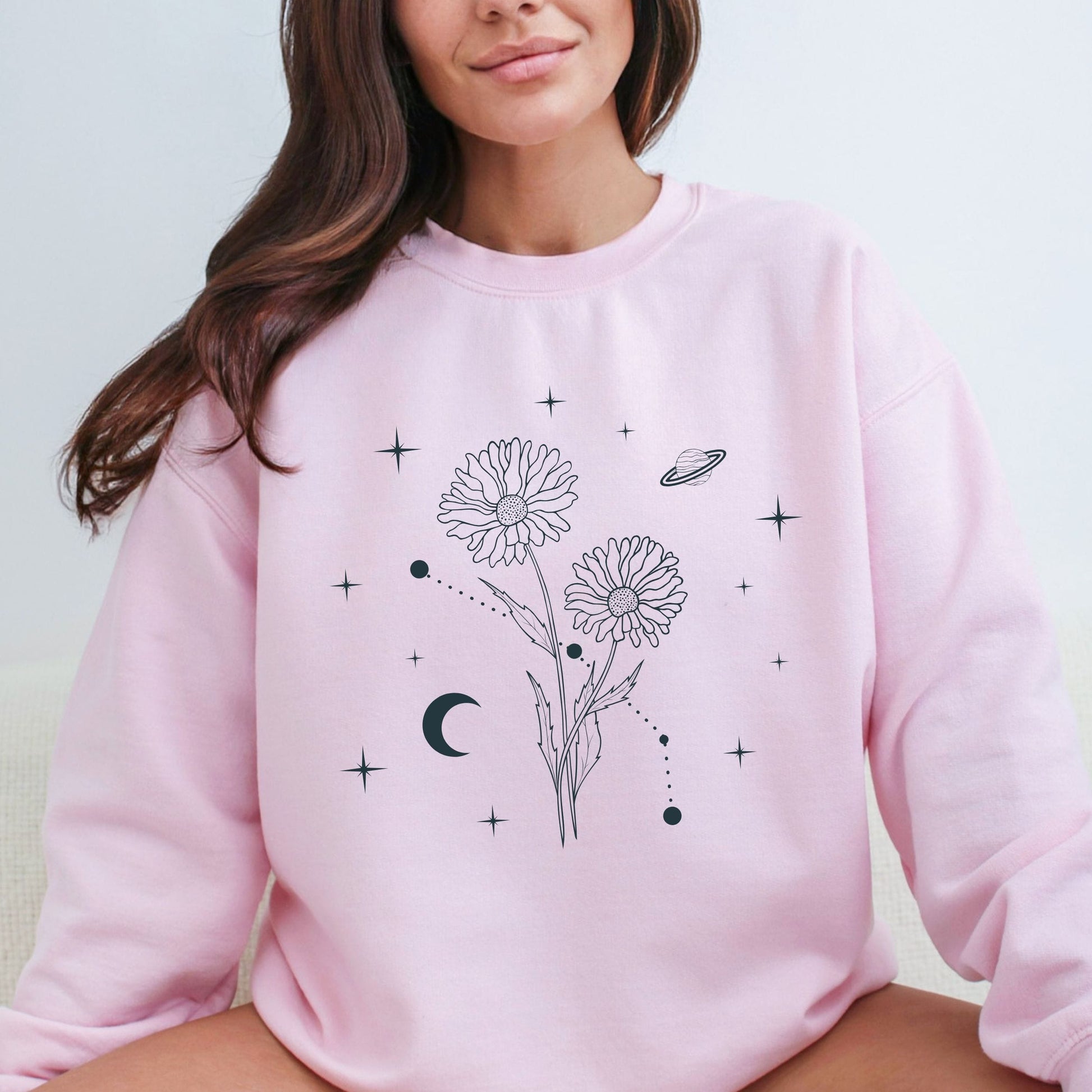 Person wearing a pink sweatshirt with floral and celestial designs.