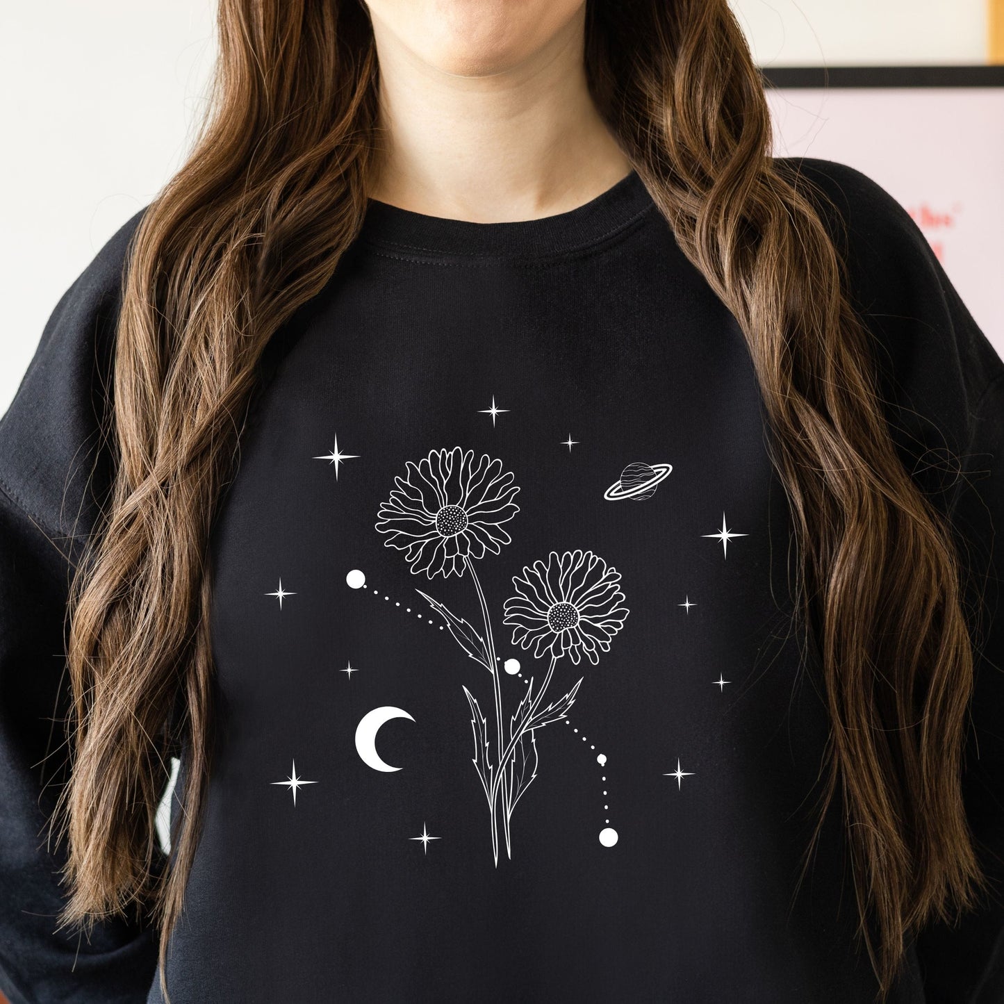 Person wearing a black sweatshirt with white floral and celestial design