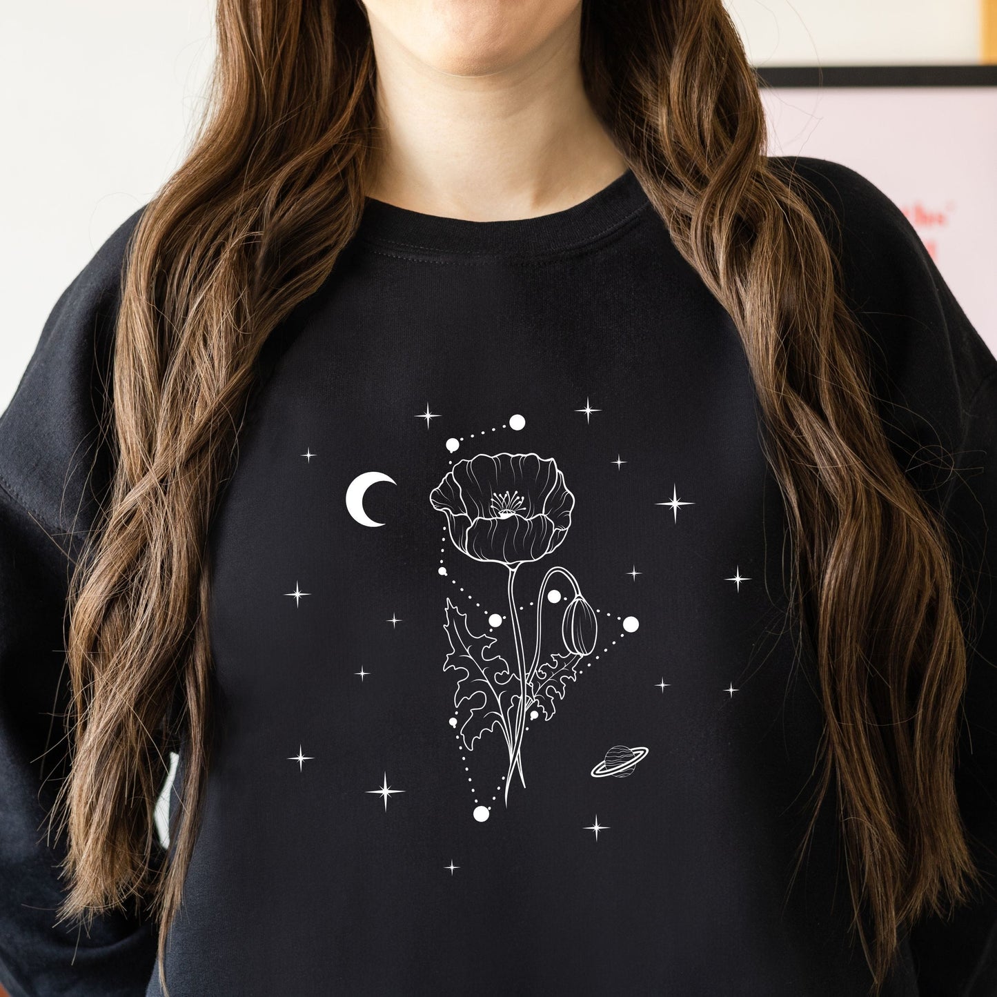Person wearing a black sweatshirt with a white floral and celestial design.