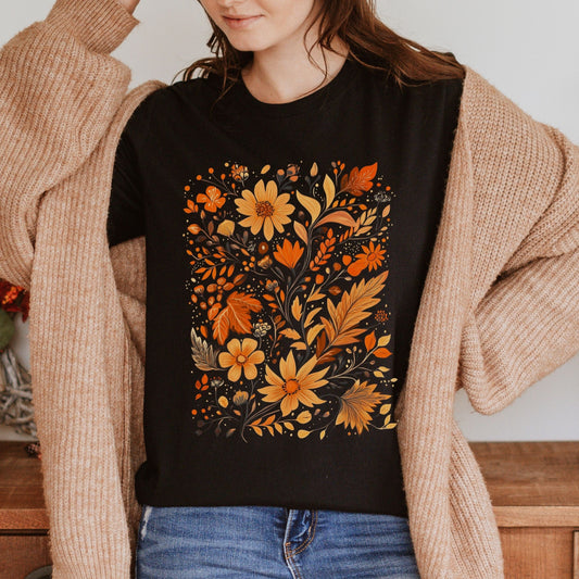 Person wearing a black t-shirt with autumn-themed floral design, standing indoors.