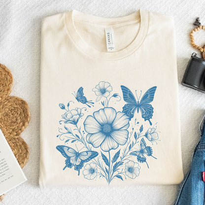 Beige t-shirt with blue floral and butterfly design on a white surface.