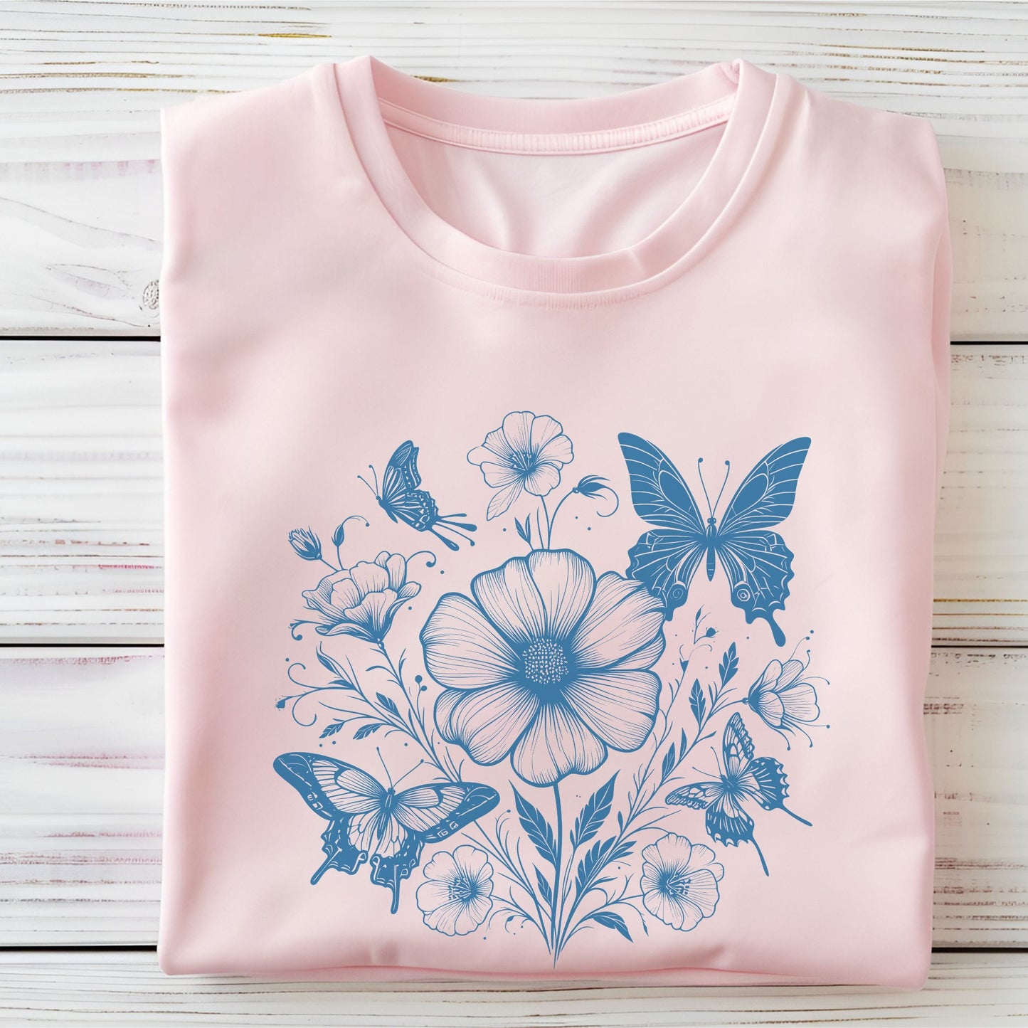 Pink t-shirt with blue floral and butterfly design on a wooden surface