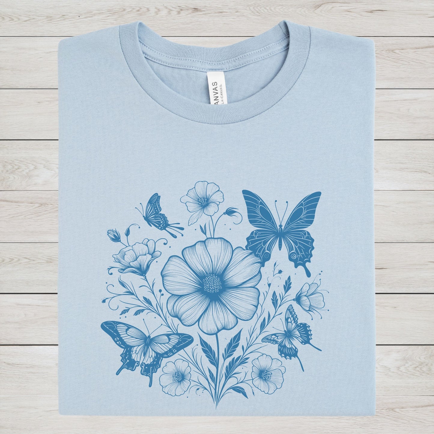 Blue t-shirt with blue floral and butterfly design on a wooden surface
