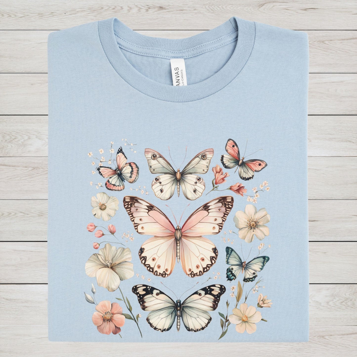 Light blue t-shirt with butterfly and flower design on a wooden surface