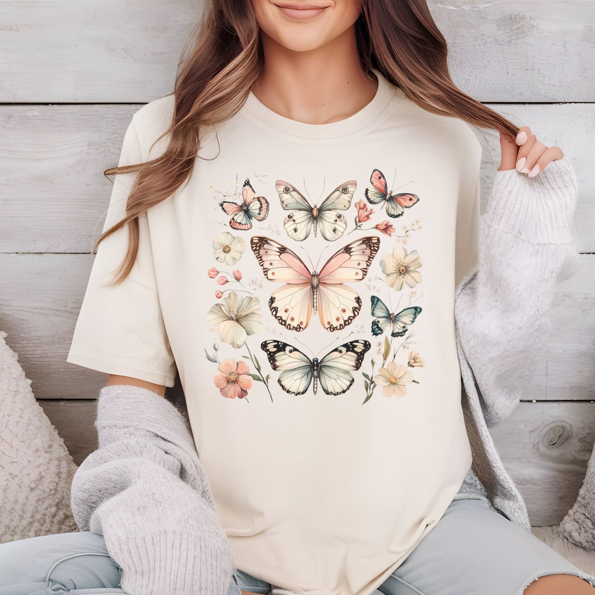 Person wearing a cream-colored sweatshirt with butterfly and floral designs, sitting against a wooden wall.