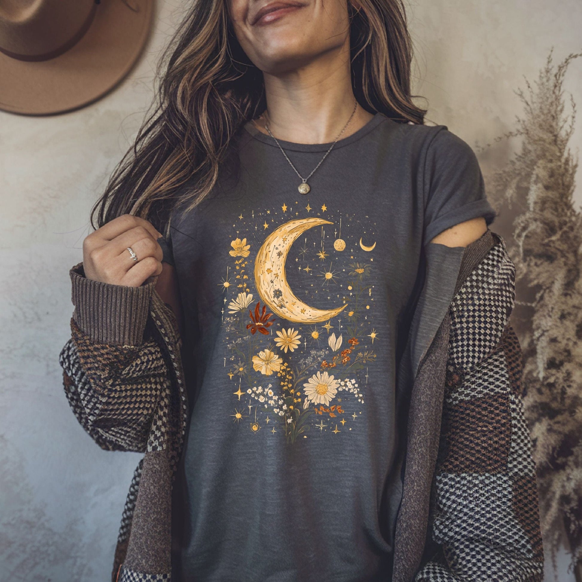 Woman wearing a dark gray t-shirt with a celestial design, holding a brown jacket.