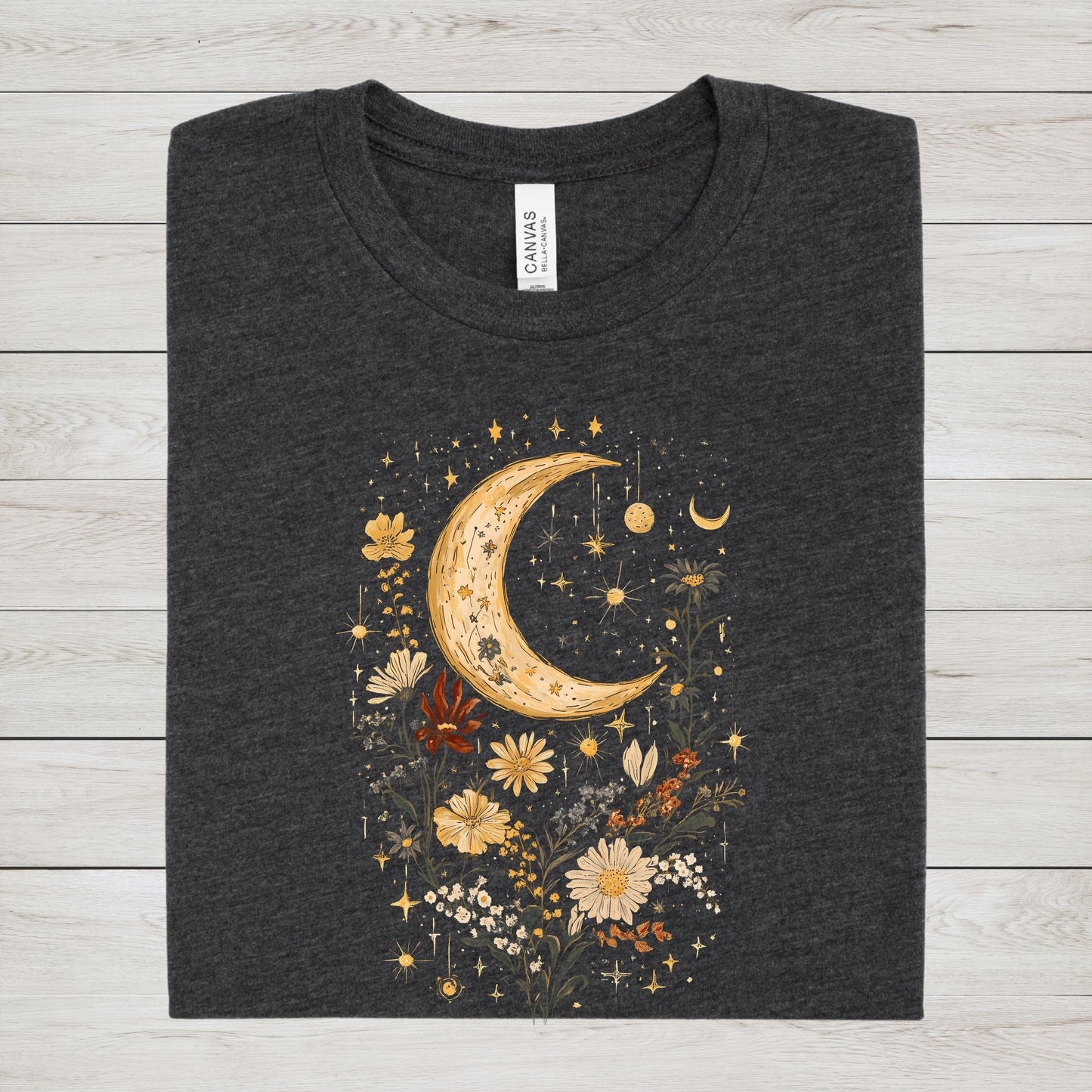 Dark gray t-shirt with a celestial design featuring a moon, stars, and flowers on a wooden surface.