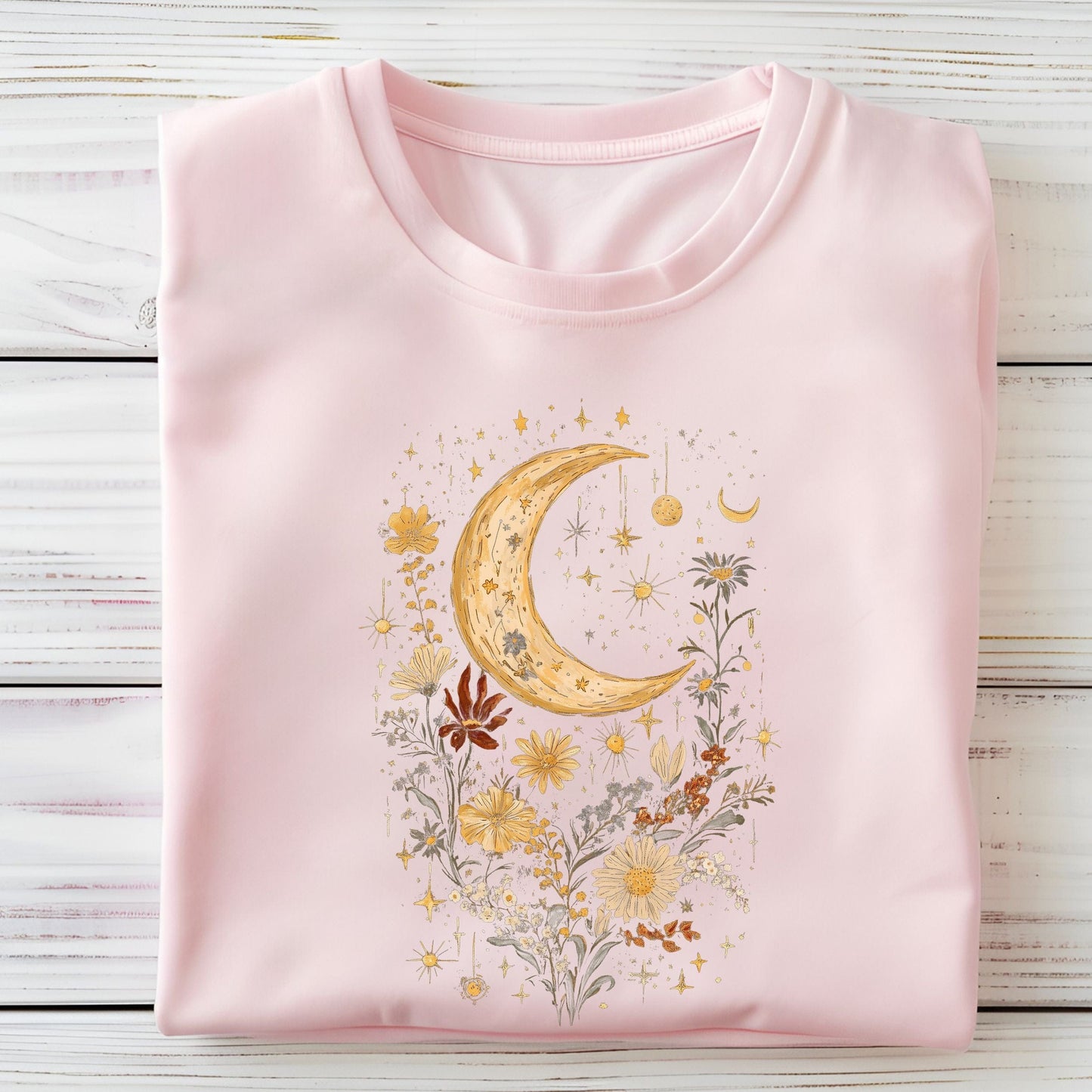 Pink t-shirt with a moon and floral design on a wooden surface