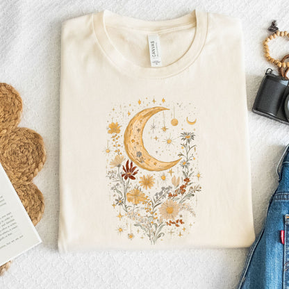 Beige t-shirt with a decorative moon and floral design on a textured surface.