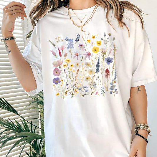 White t-shirt with floral design worn by a person, with a plant in the background.