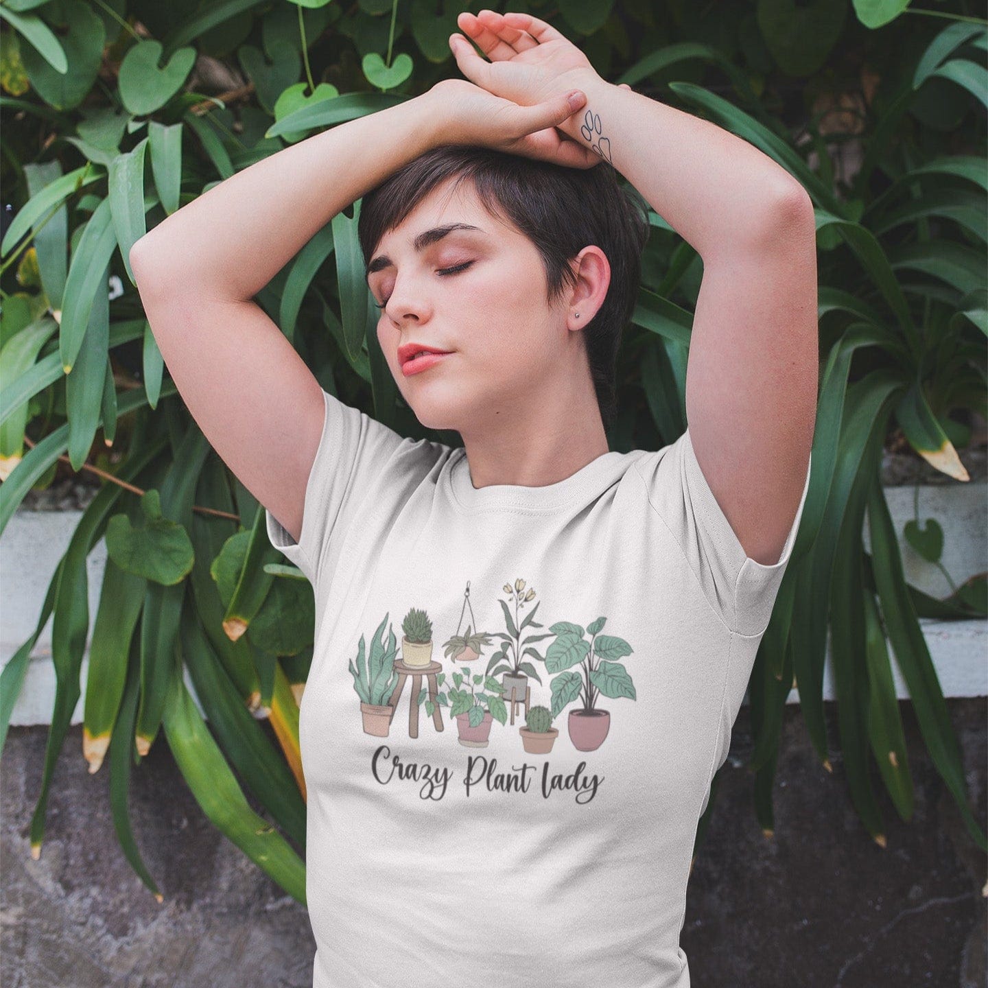 Person wearing a t-shirt with plant illustrations and text, standing in front of green foliage.