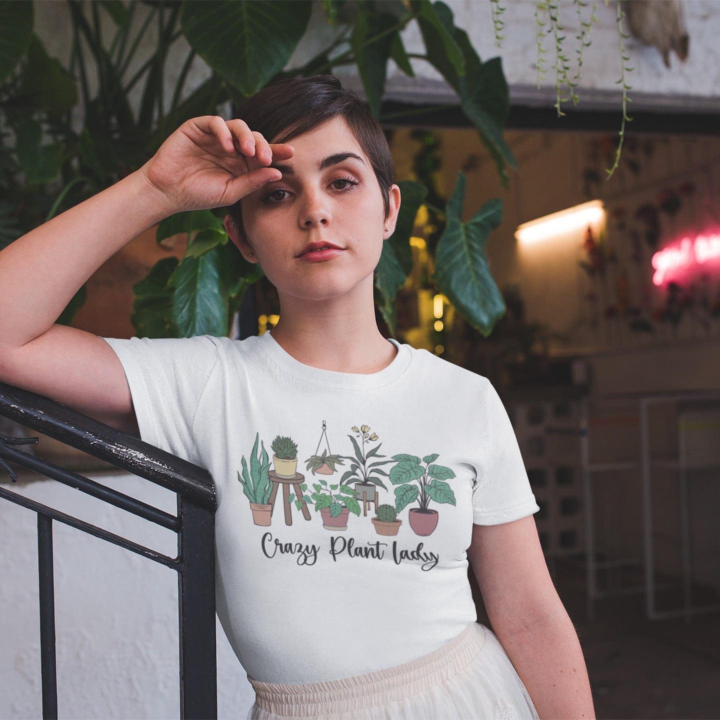 Person wearing a t-shirt with plant designs and text, standing indoors with plants in the background.