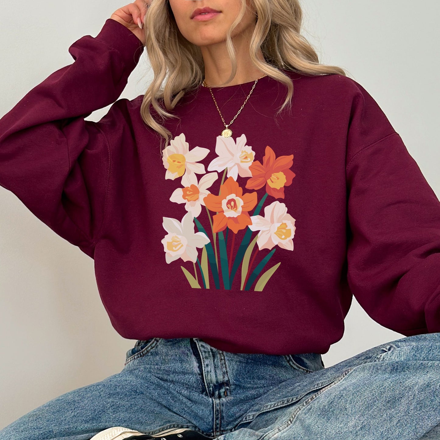 Person wearing a maroon sweatshirt with floral design and blue jeans against a plain background