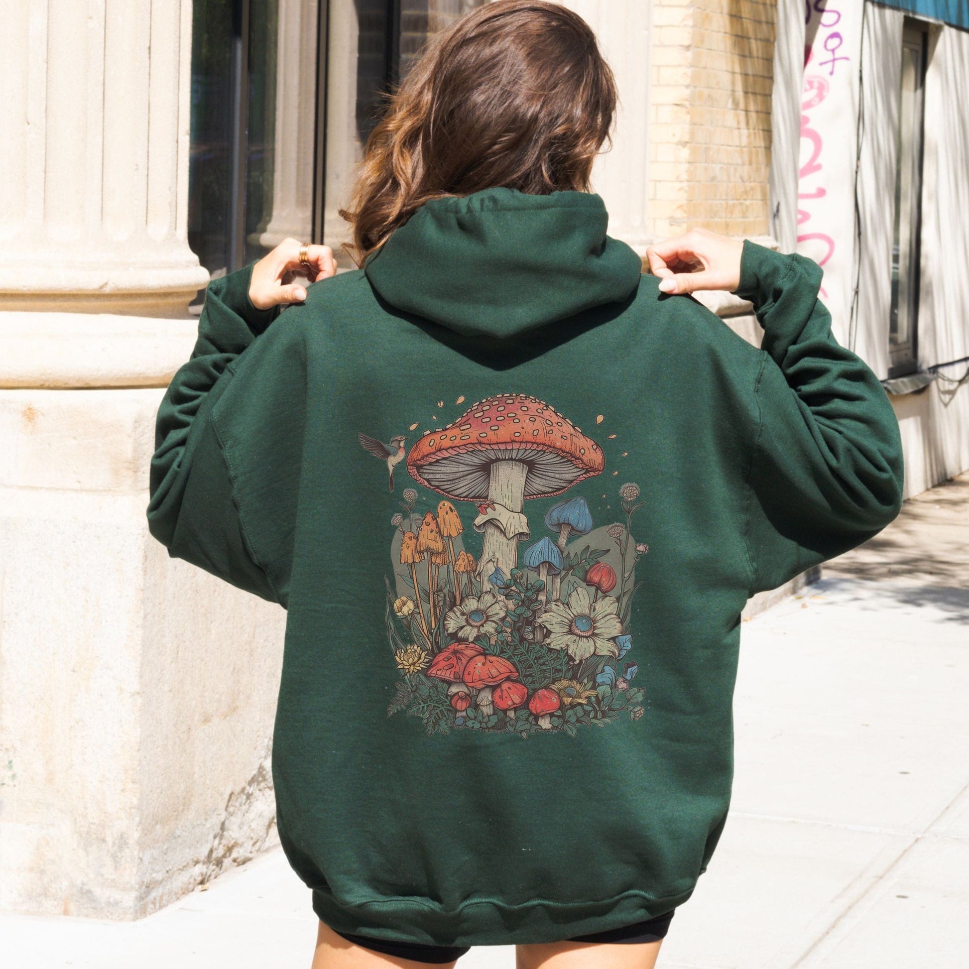 Person wearing a green hoodie with a mushroom design on the back, standing outdoors.