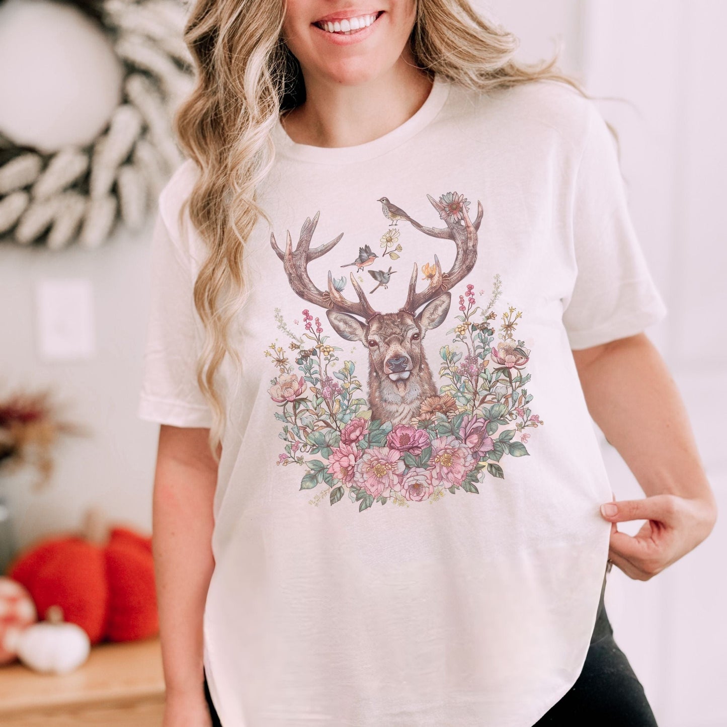 Woman wearing a white t-shirt with a deer and floral design, standing in a cozy indoor setting.