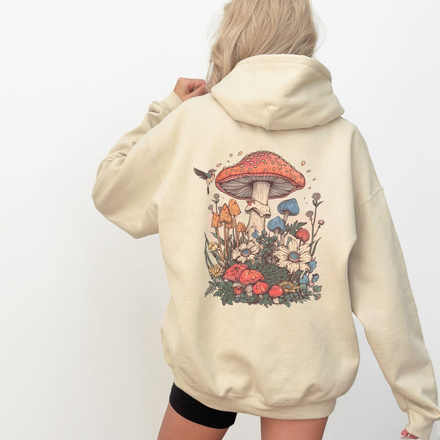Person wearing a beige hoodie with a colorful mushroom design on the back against a white background