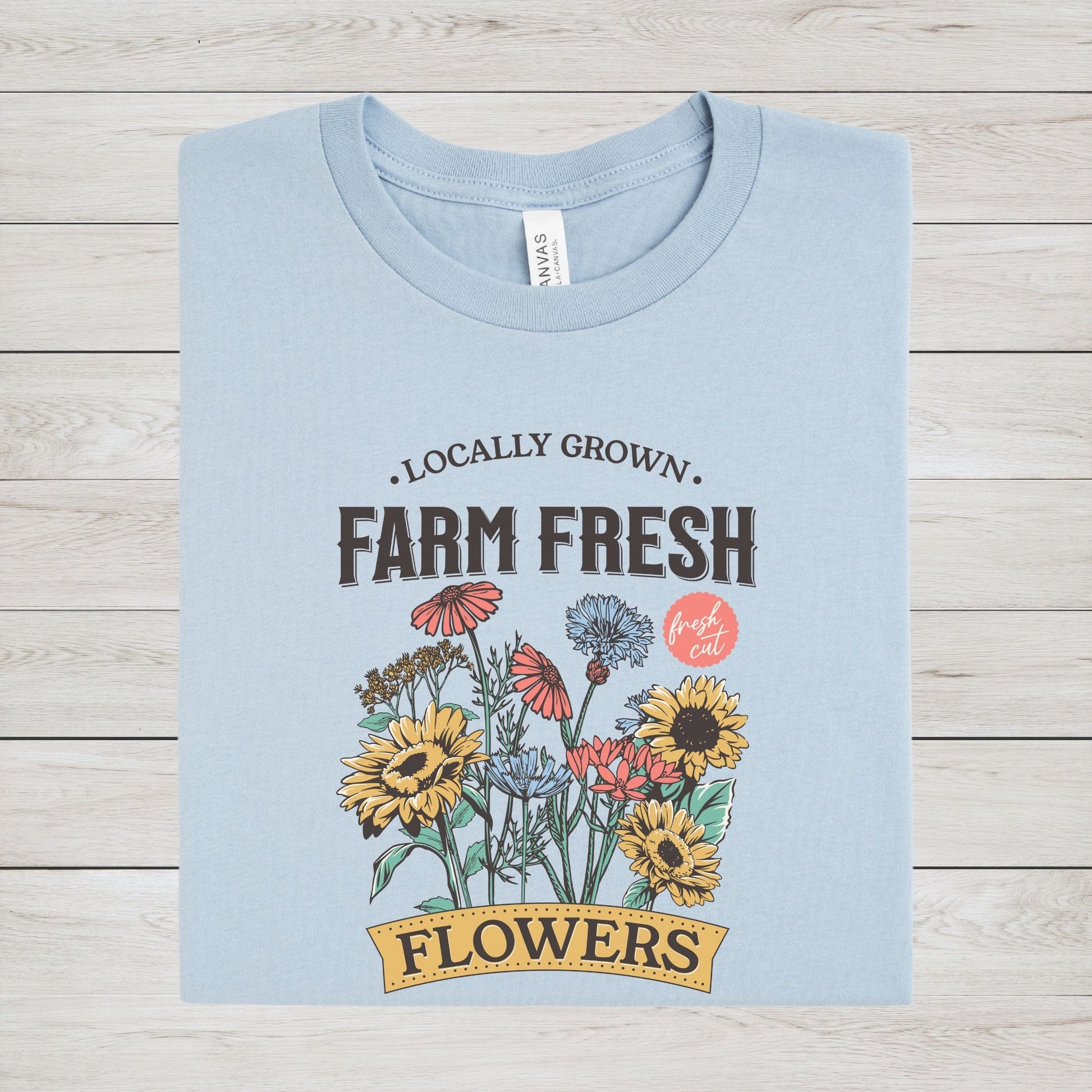Light blue t-shirt with 'Farm Fresh Flowers' graphic on a wooden surface
