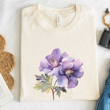 Folded cream-colored t-shirt with a purple floral design on a textured surface.