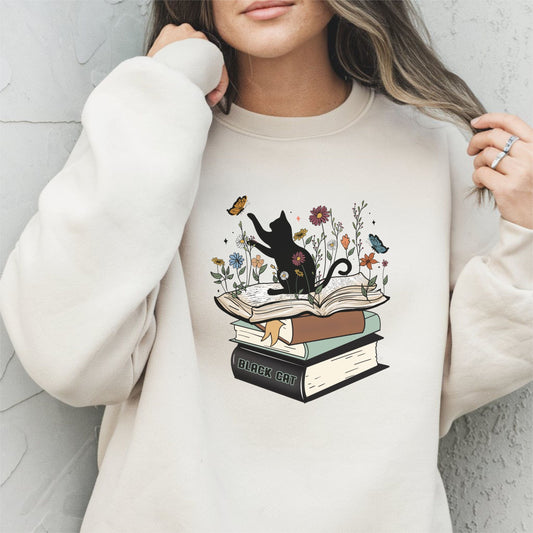 Person wearing a beige sweatshirt with a black cat and books design.