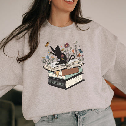 Person wearing a gray sweatshirt with a black cat and books design.