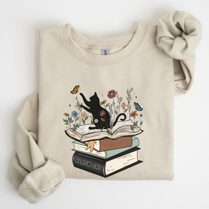Beige sweatshirt with a graphic of a cat on books and flowers on a white background