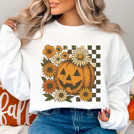 Person wearing a white sweatshirt with a pumpkin and floral design, sitting in front of a 'fall' pillow.