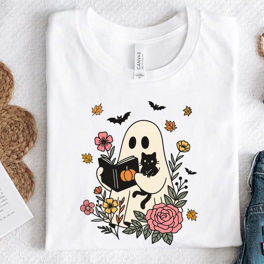 White t-shirt with a ghost holding a book and surrounded by flowers on a textured surface.
