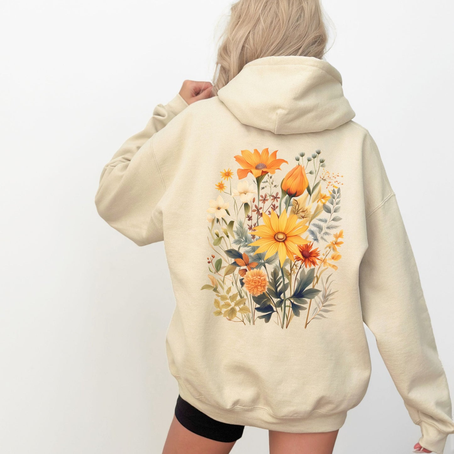 A woman shown from the back wearing a cream-colored hoodie with a large, colorful watercolor-style floral print on the back. The background is a clean, solid white.