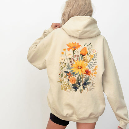 A woman shown from the back wearing a cream-colored hoodie with a large, colorful watercolor-style floral print on the back. The background is a clean, solid white.