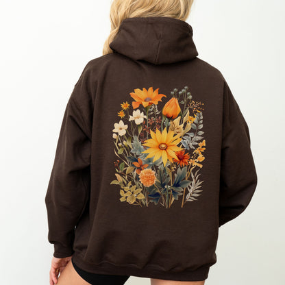 A person viewed from the back wearing a dark brown pullover hoodie with a large, colorful floral graphic printed on the back. The design features yellow, orange, and white flowers with green and brown leaves.