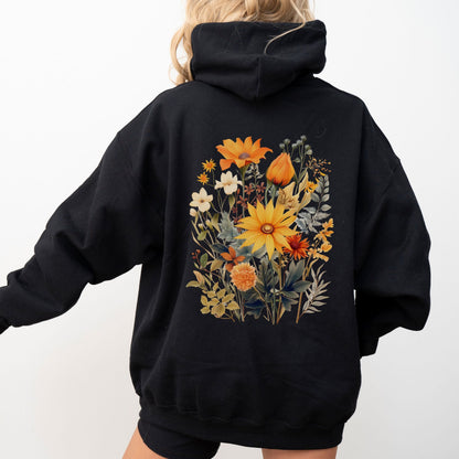 A person wearing an oversized black hoodie from the back, featuring a large colorful floral print with yellow, orange, and white flowers on the back, set against a plain white background.