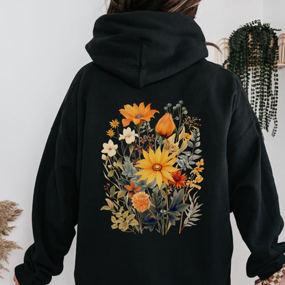 A person wearing a black hoodie, viewed from the back, featuring a large colorful floral print with yellow, orange, and white flowers on the back.