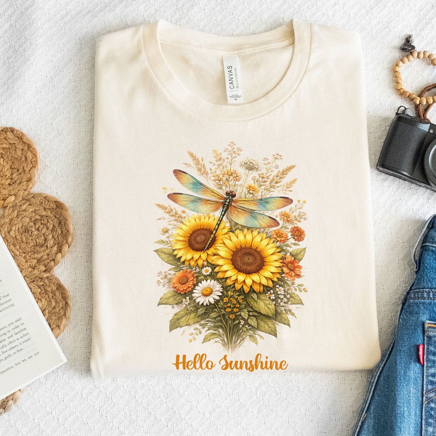 Beige t-shirt with floral design and 'Hello Sunshine' text on a textured surface.
