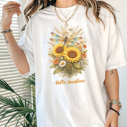 White t-shirt with floral design and 'Hello Sunshine' text worn by a person, with a plant in the background.