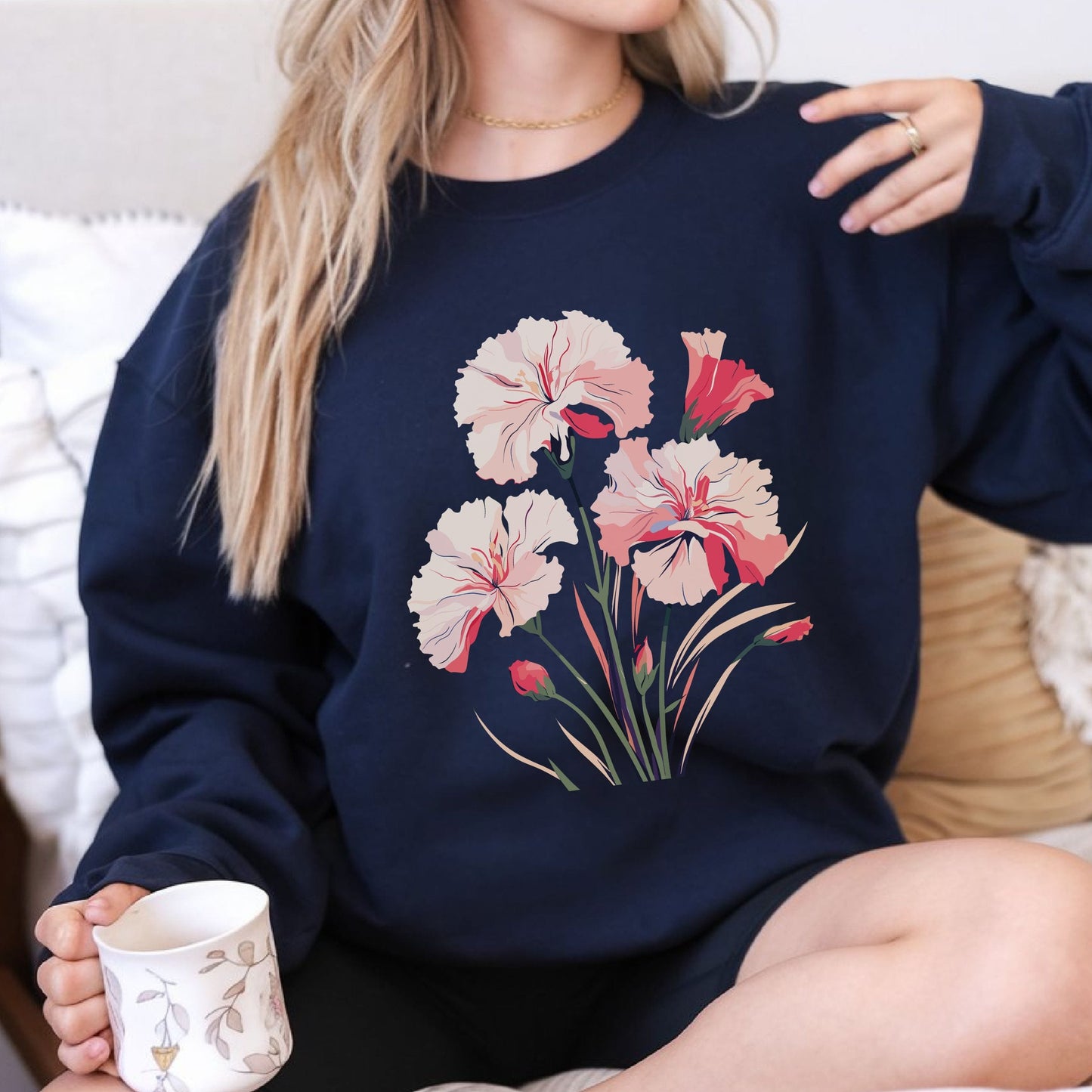 Person wearing a navy sweatshirt with floral design, holding a mug.