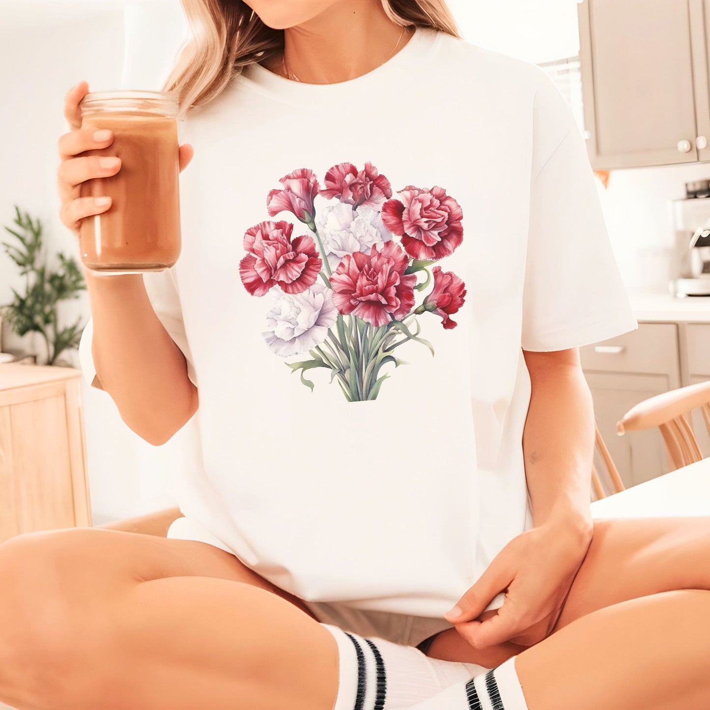 Person wearing a white t-shirt with a floral design, holding a coffee cup.