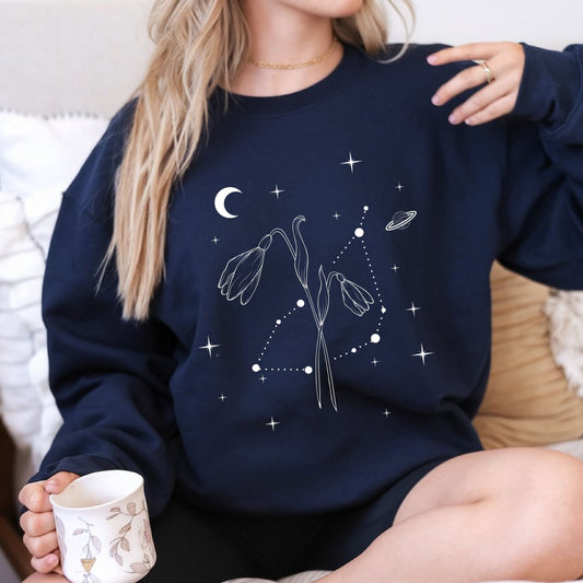 Person wearing a navy blue sweatshirt with celestial design, holding a mug.